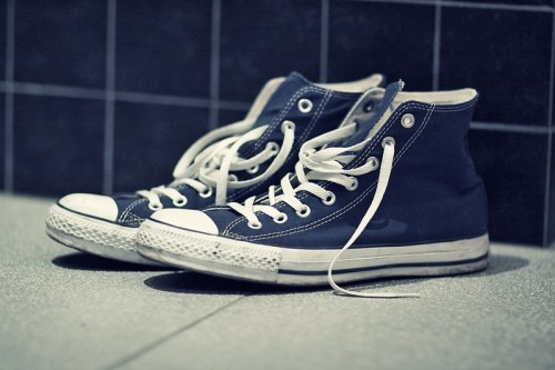A pair of worn blue high-top sneakers with white laces, resting on a tiled floor.