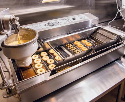 A commercial donut fryer with donuts cooking in a stainless steel machine.