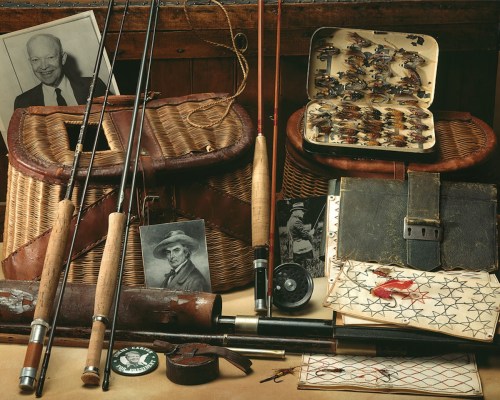A collection of fishing gear, including rods, flies, and photographs, arranged on a wooden surface.