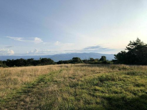 A scenic view of rolling mountains under a clear sky, with a grassy field in the foreground.