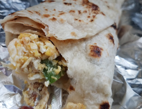 A close-up of a wrapped burrito with scrambled eggs and green peppers, partially unwrapped on foil.