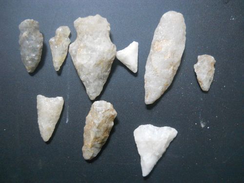 A collection of various stone arrowheads and tools arranged on a dark surface.