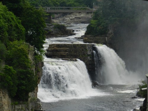 A scenic view of cascading waterfalls surrounded by lush greenery and rocky cliffs.