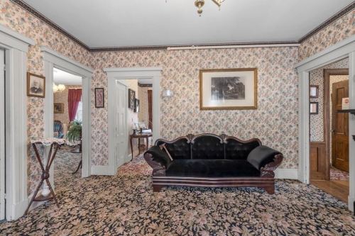 A vintage living room with floral wallpaper, a black sofa, and ornate decor, featuring doorways to adjacent rooms.