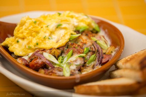 A dish featuring scrambled eggs, sautéed onions, and potatoes, served with toasted bread on the side.