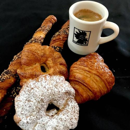 A variety of pastries including croissants and a donut, alongside a cup of coffee on a black surface.