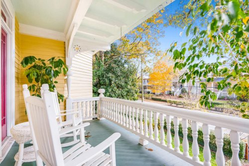 A cozy porch with rocking chairs, surrounded by greenery and autumn trees under a clear blue sky.