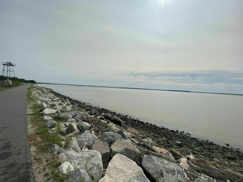 A calm river scene with rocky shoreline and a path, under a cloudy sky.