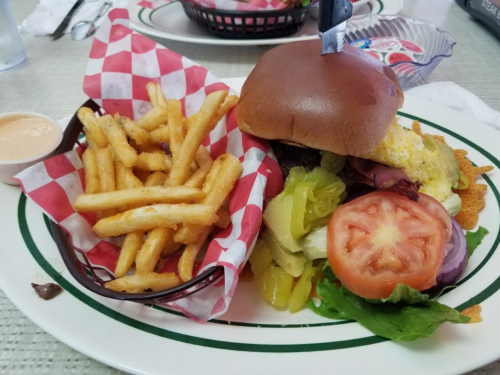 A juicy burger with toppings and a side of crispy fries in a basket, served on a plate with checkered paper.