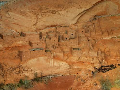 Ancient cliff dwellings nestled in a rocky landscape, showcasing adobe structures against a reddish-brown backdrop.
