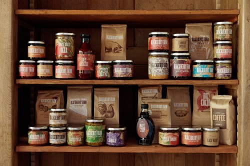 A wooden shelf displaying various jars and bags of food products, including jams, sauces, and coffee.