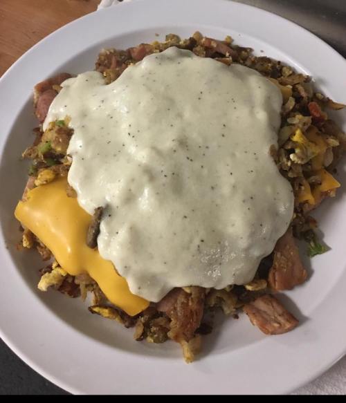 A plate of hash with diced meats, vegetables, and melted cheese, topped with a creamy white sauce.