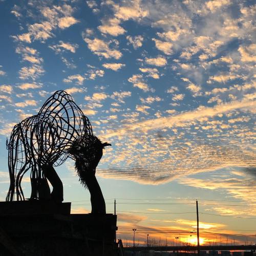 Silhouette of a horse sculpture against a colorful sunset and cloudy sky.