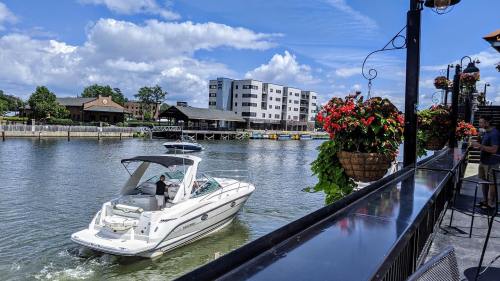 A boat navigates a calm river with buildings and flower baskets lining the waterfront under a blue sky.