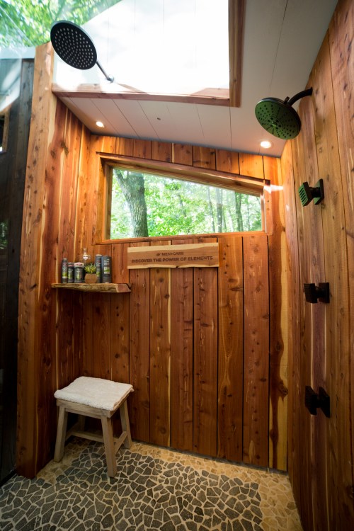 A wooden shower with natural light, featuring a bench, shelves, and a view of trees through a window.