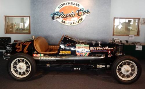 A vintage 1929 Ford racer displayed in a classic car museum, featuring a black body and brown leather interior.