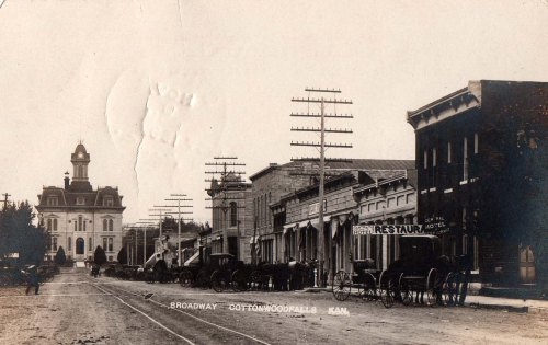 Historic street scene in Cottonwood Falls, Kansas, featuring horse-drawn carriages and early 20th-century buildings.