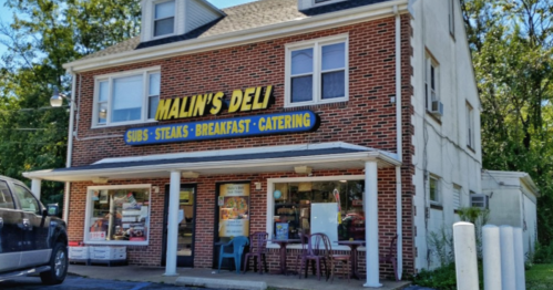 A brick building with a sign reading "Malin's Deli" offering subs, steaks, breakfast, and catering services.