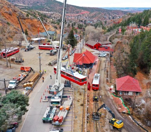 Aerial view of a construction site with cranes, red buildings, and workers in a mountainous area.