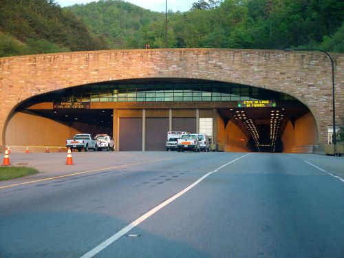 Entrance to the Cumberland Gap Tunnel, flanked by vehicles and traffic cones, surrounded by green hills.