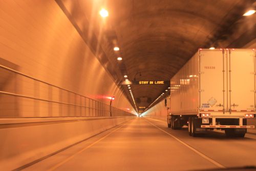 A truck drives through a well-lit tunnel with a "STAY IN LANE" sign visible ahead.