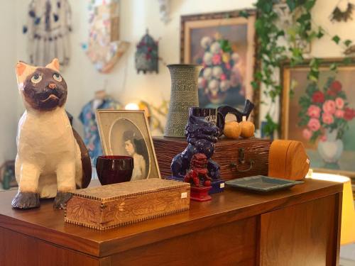 A display of vintage items including a ceramic cat, a vase, a framed portrait, and decorative boxes on a wooden table.