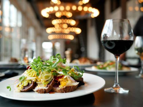 A beautifully plated dish with colorful vegetables and meat, accompanied by a glass of red wine in a stylish setting.