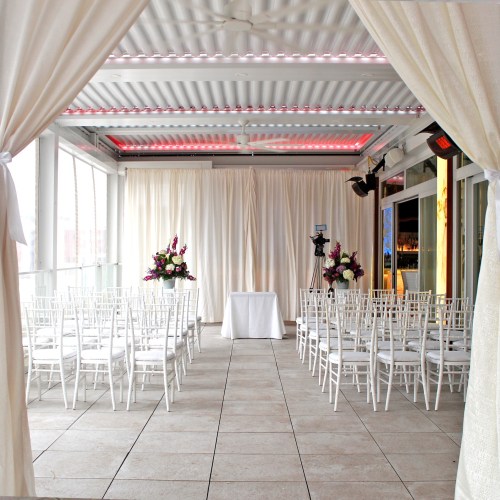 A decorated indoor venue with white chairs arranged for a ceremony, featuring floral arrangements and soft lighting.