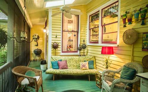 Cozy porch with yellow walls, a green sofa, colorful decor, and a ceiling fan, creating a welcoming atmosphere.