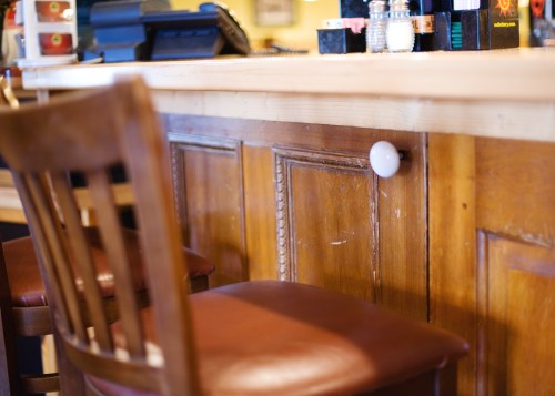A wooden bar with a polished surface, featuring a brown leather chair and a small white light fixture on the side.