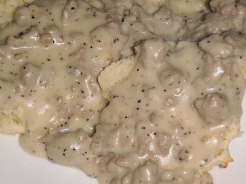 A close-up of creamy sausage gravy poured over fluffy biscuits, with a peppery texture.