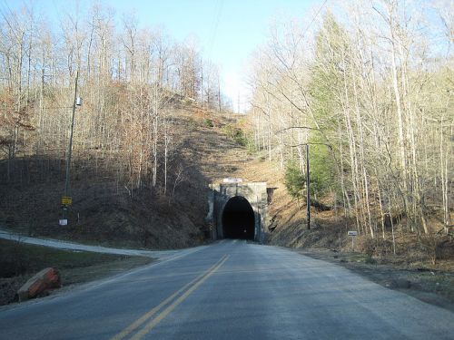 A road leading to a dark tunnel surrounded by bare trees and a hilly landscape on a clear day.