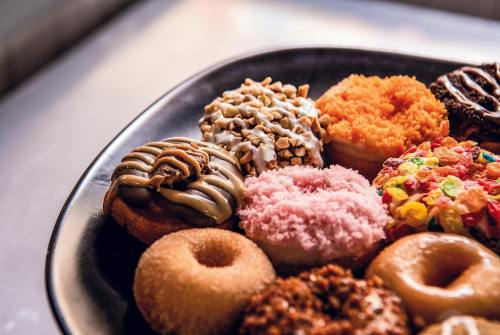 A variety of colorful donuts on a black plate, featuring toppings like sprinkles, nuts, and frosting.