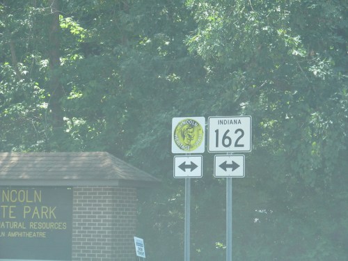 Sign for Lincoln State Park in Indiana, with route number 162 and directional arrows. Green trees in the background.