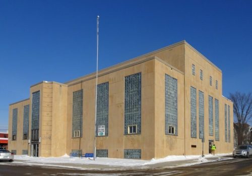 A large, beige Art Deco building with glass block windows, set against a clear blue sky and snow-covered ground.