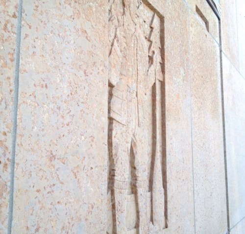 Relief sculpture of a figure carved into a textured stone wall, showcasing intricate details and patterns.