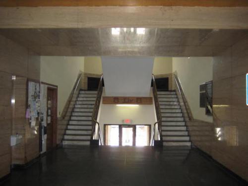 Interior view of a building's entrance with two staircases leading to upper floors and a large window at the end.