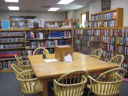 A cozy library with wooden shelves filled with books and a large table surrounded by chairs.