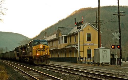 A train approaches the Thurmond station, with mountains in the background and signal lights indicating track status.