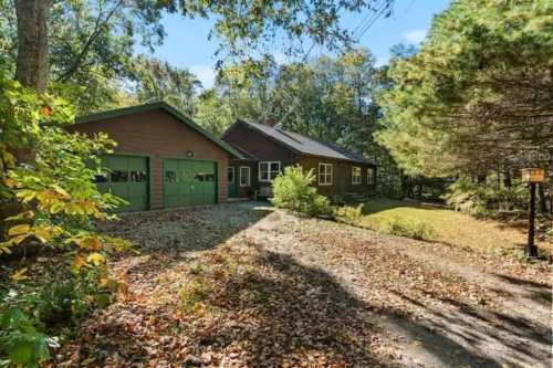 A cozy brown house with a green garage, surrounded by trees and autumn leaves on a sunny day.