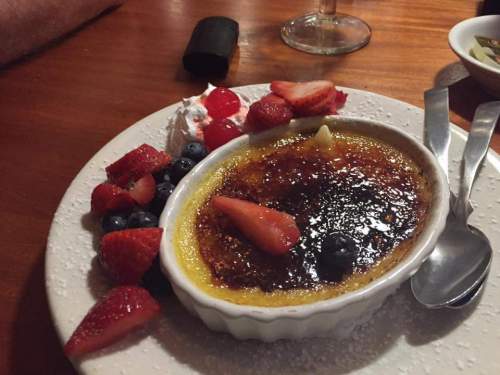 A creamy crème brûlée topped with caramelized sugar, garnished with fresh strawberries, blueberries, and whipped cream.