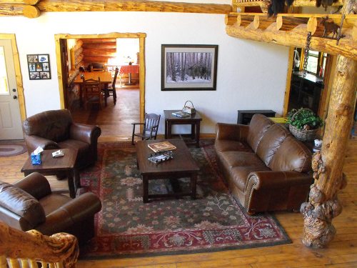 Cozy living room with leather sofas, a wooden coffee table, and rustic decor, featuring a view into a dining area.