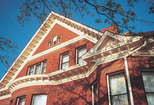 A close-up of a red brick house with decorative white trim and a clear blue sky in the background.