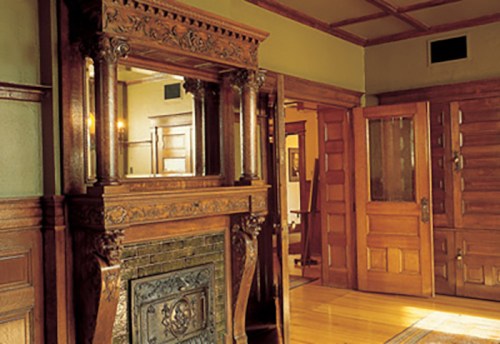 A vintage room featuring ornate wooden details, a decorative fireplace, and a large mirror reflecting the space.