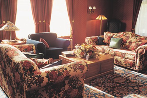 Cozy living room with floral-patterned sofas, a wooden coffee table, and warm lighting from a lamp.