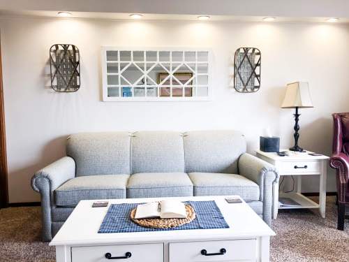 Cozy living room with a gray sofa, coffee table, and decorative wall mirrors, featuring warm lighting and a neutral color palette.
