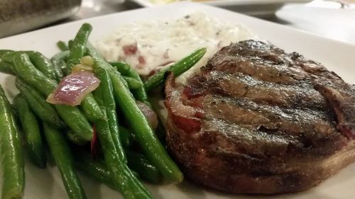 A plate featuring grilled steak, green beans, and creamy rice with herbs.
