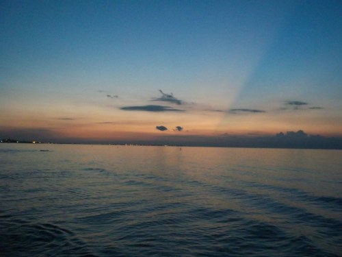 A serene ocean view at dusk, with soft waves reflecting the colorful sky and distant lights along the horizon.