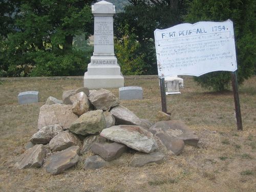 A pile of rocks in front of a historical marker and a sign about Fort Pearsall, surrounded by grass and trees.