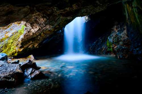 A serene waterfall cascades into a tranquil pool, surrounded by rocky cave walls and lush greenery.